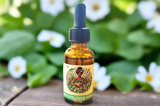 a bottle of spearmint flower essence from Mama Gaia's Medicinals is on a wooden table with a backdrop of spearmint growing and flowering.
